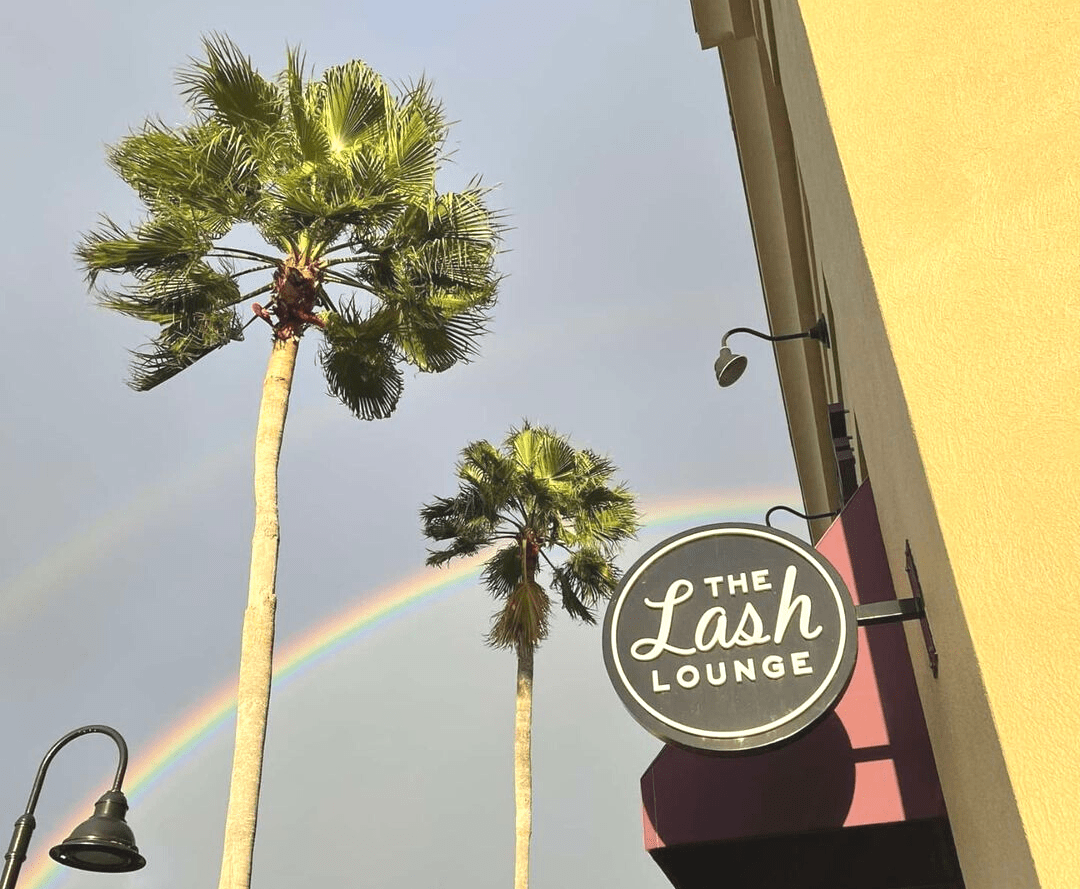 A rainbow over The Lash Lounge franchise with palm trees.